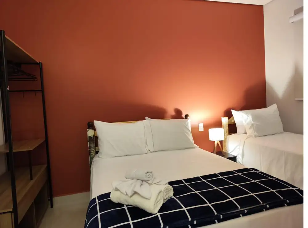 Suíte com cama de casal, cama de solteiro e parede terracota